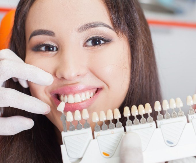 Young woman smiling while cosmetic dentist holds shade guide near her smile