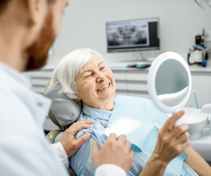 Senior dental patient admiring her smile in mirror