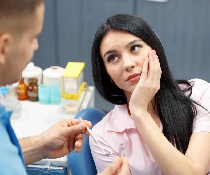 Woman holding her cheek in pain while talking to emergency dentist