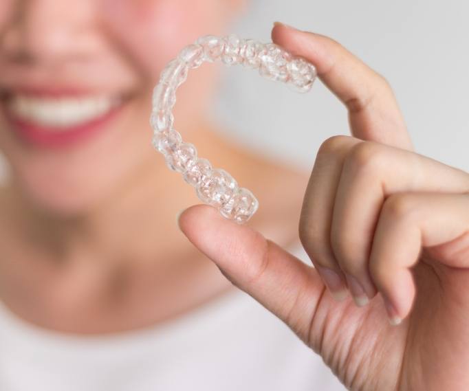 Smiling person holding an Invisalign aligner
